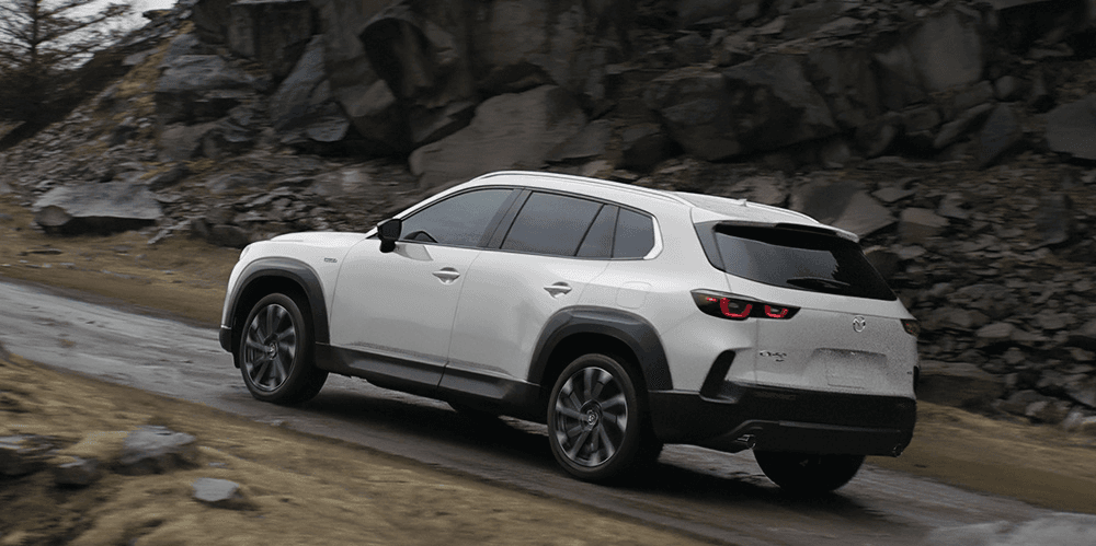 Vue 3/4 latérale du Mazda CX-50 hybride 2025 roulant sur un chemin de terre.